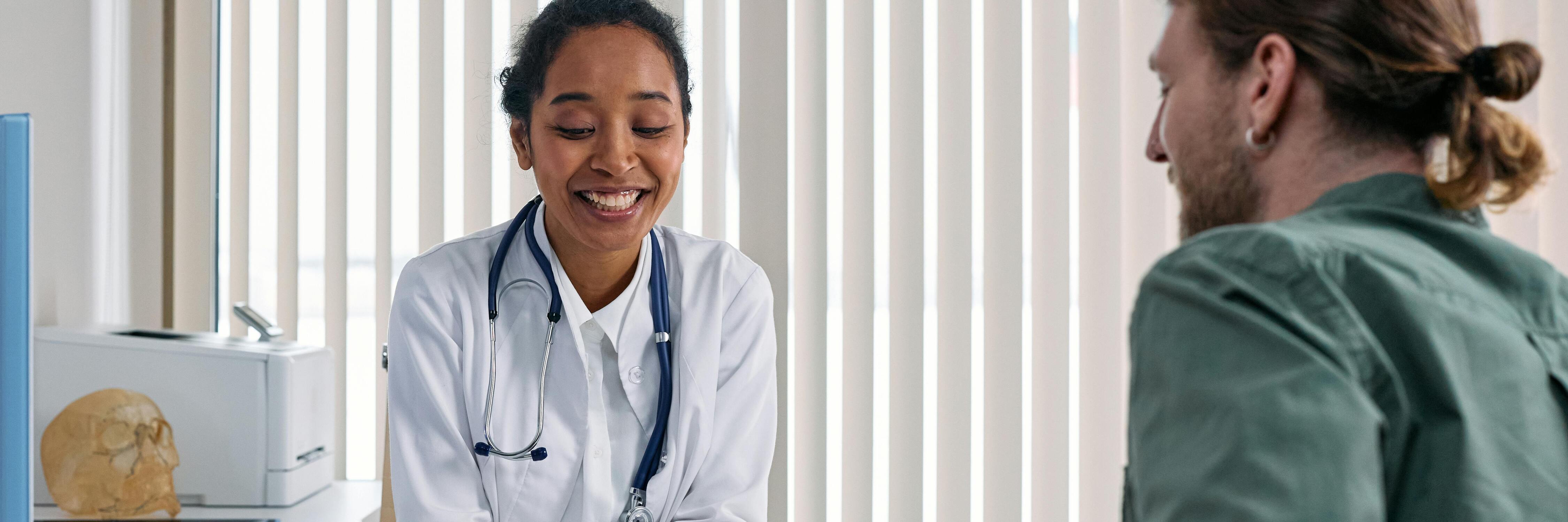 Doctor smiling and looking at clipboard while talking to patient across table