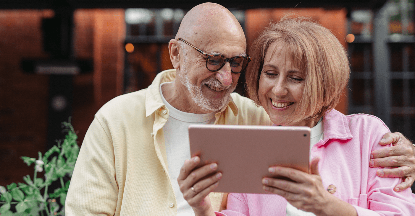 Male and female couple smiling while reading tablet that woman is holding