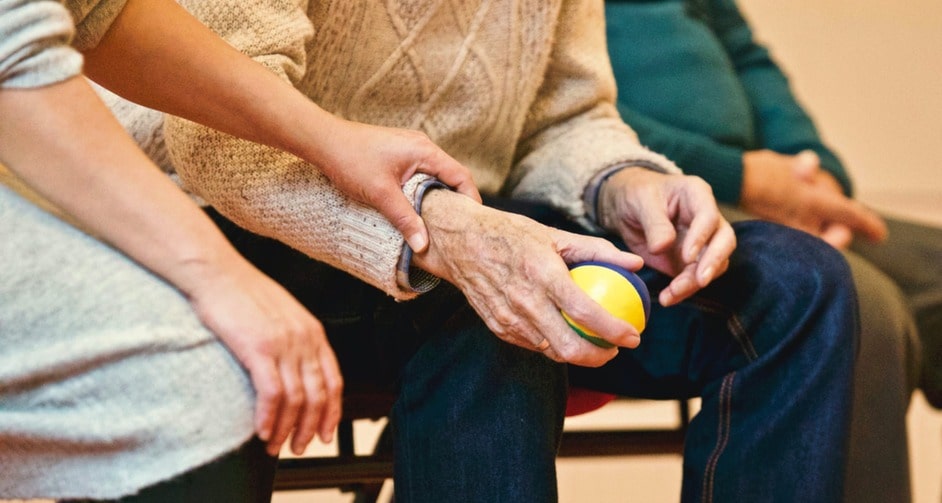 Old man sitting down holding stress ball with two people sitting on either side of him